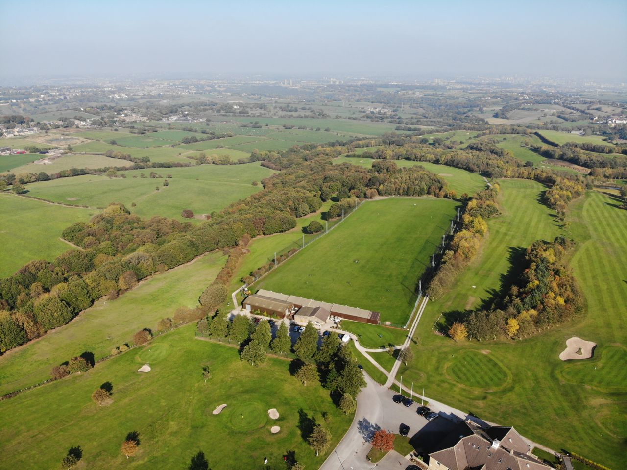 An aerial photo showing the driving range at The Manor, Drighlington, along with the surrounding golf course and farm land. It is a sunny days and the trees are in leaf.